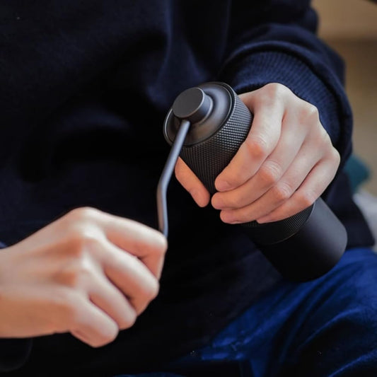 Person holding a black coffee maker with a spoon